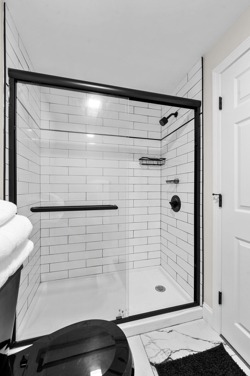 A modern shower room with white tiled walls, a glass door, and a black shower head.
