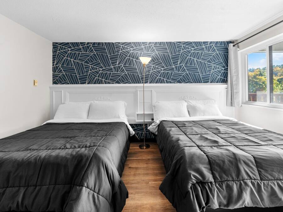 Ein Schlafzimmer mit zwei Betten, einer Wand mit Muster, einer Stehlampe und einem Fenster mit Blick.