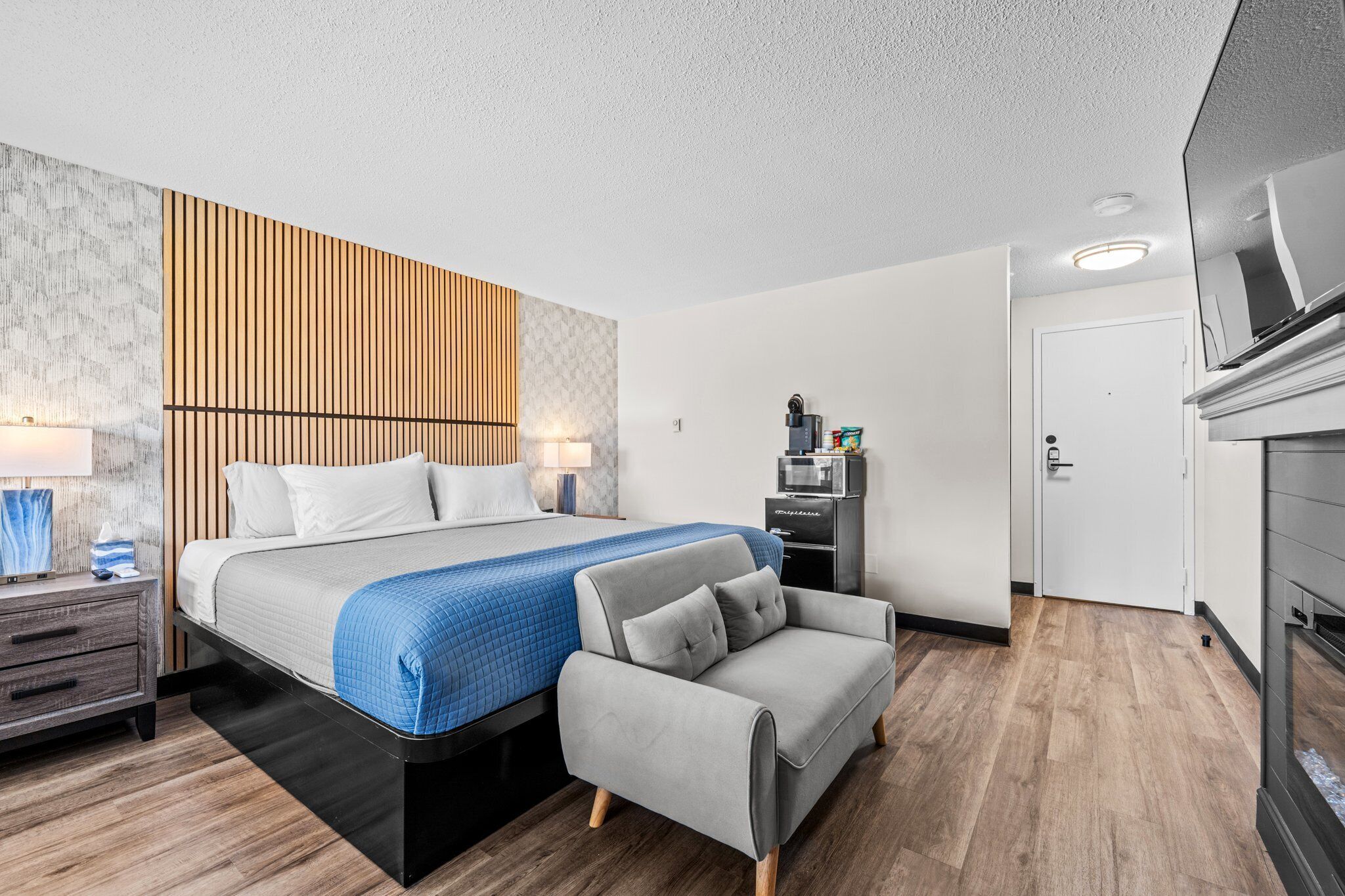 A modern hotel room with a bed, a sofa, a desk, and a TV.