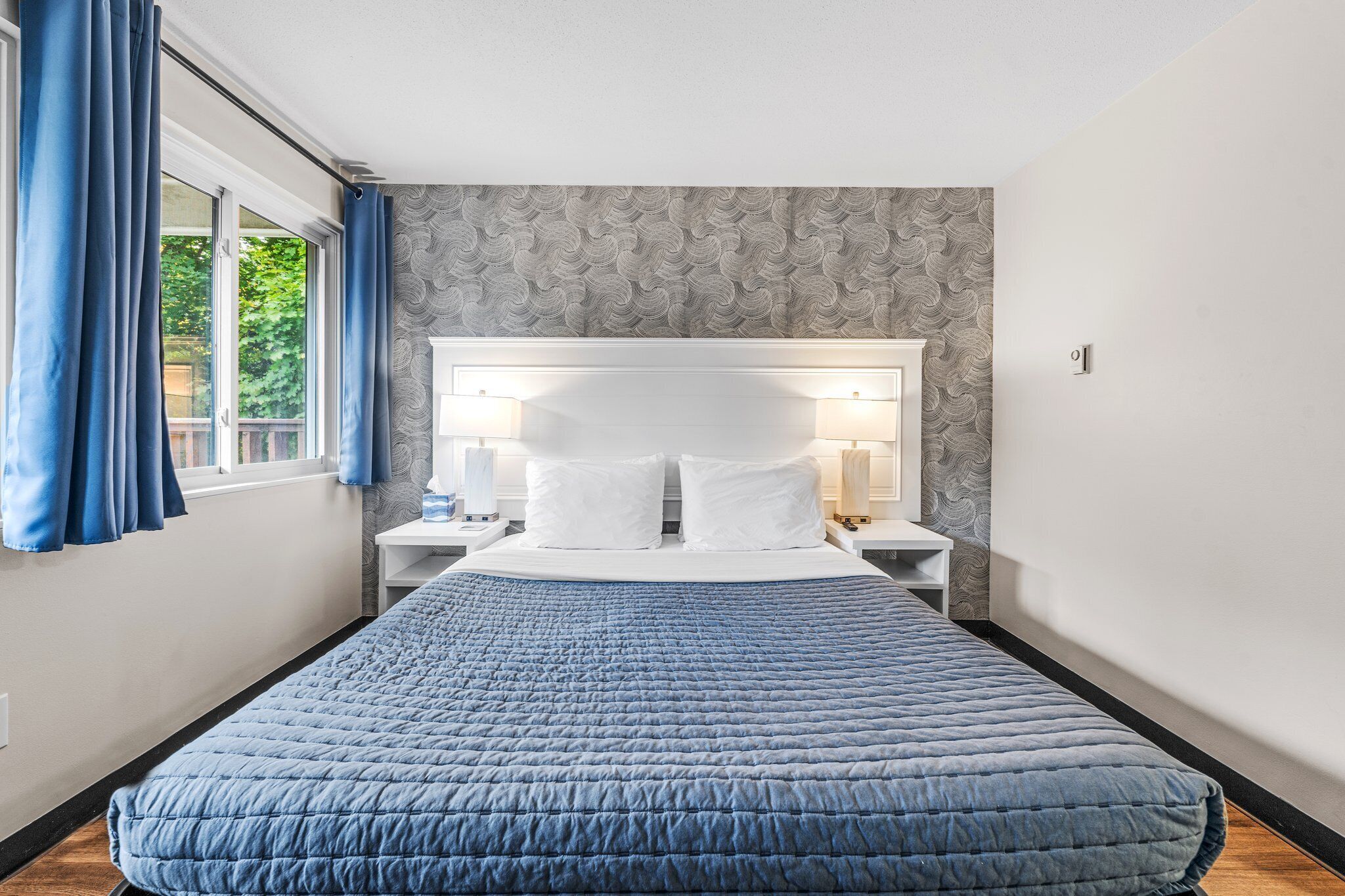 A neatly made bed with a blue quilt, a white headboard, and two bedside tables with lamps.