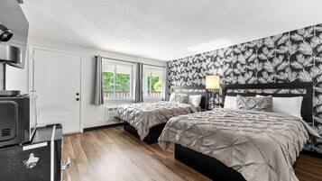 A hotel room with two beds, a kitchenette, and a window with a view of greenery.