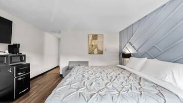 A modern bedroom with a large bed, a flat-screen TV, a coffee maker, and a painting on the wall.