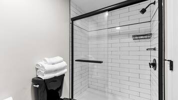 Un baño moderno con ducha separada por vidrio, paredes de azulejos blancos y un inodoro negro.