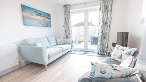 Ein modernes Wohnzimmer mit einem hellblauen Sofa, einem grauen Sofa und einem Couchtisch. Es gibt ein großes Fenster mit Vorhängen, eine Heizung und ein Gemälde an der Wand.