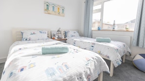 Ein Schlafzimmer mit zwei Betten, einem Fenster mit Vorhängen, einem kleinen Tisch mit Lampe und einem Bild an der Wand.