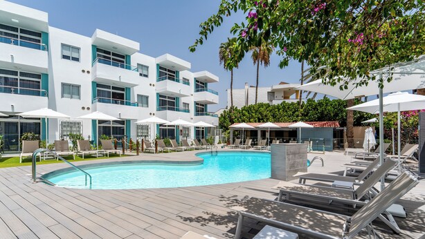 Un hotel moderno con zona de piscina, sillas de descanso y sombrillas.