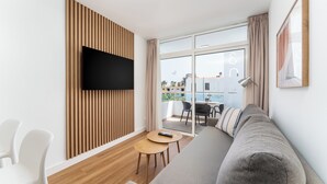 Un moderno salón con una televisión de pantalla plana, un sofá, una mesita redonda y un balcón con vistas.