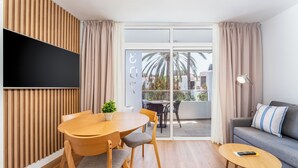 Una sala de estar moderna con un revestimiento de madera, un televisor de pantalla plana, un sofá gris con almohadones a rayas, una mesa de centro redonda de madera y un comedor con mesa y sillas de madera.