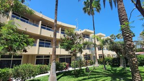 Un hotel de varios pisos con balcones, rodeado de palmeras y césped cuidado.