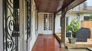 A covered outdoor area with a tiled walkway leading to a door, surrounded by a wooden deck and outdoor furniture. - A 15 Minutes des Plages, Maison de Ville Avec Petit Jardin Pour 8 Personnes (Lesparre-Médoc)