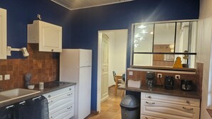 A compact kitchen with a refrigerator, stove, and a sink. There is a trash bin and a window with a view of the outside. - A 15 Minutes des Plages, Maison de Ville Avec Petit Jardin Pour 8 Personnes (Lesparre-Médoc)
