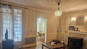 A living room with a fireplace, a dining area, and a view of the outdoors. - A 15 Minutes des Plages, Maison de Ville Avec Petit Jardin Pour 8 Personnes (Lesparre-Médoc)