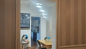 An interior view of a room with a dining area, a kitchen in the background, and a door leading to another room. - A 15 Minutes des Plages, Maison de Ville Avec Petit Jardin Pour 8 Personnes (Lesparre-Médoc)