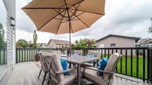 An outdoor patio with a table and chairs, an umbrella, and a view of a residential area. - Luxurious & Cozy-5bdrm Home-Minutes to WEM-WIFI (Edmonton)