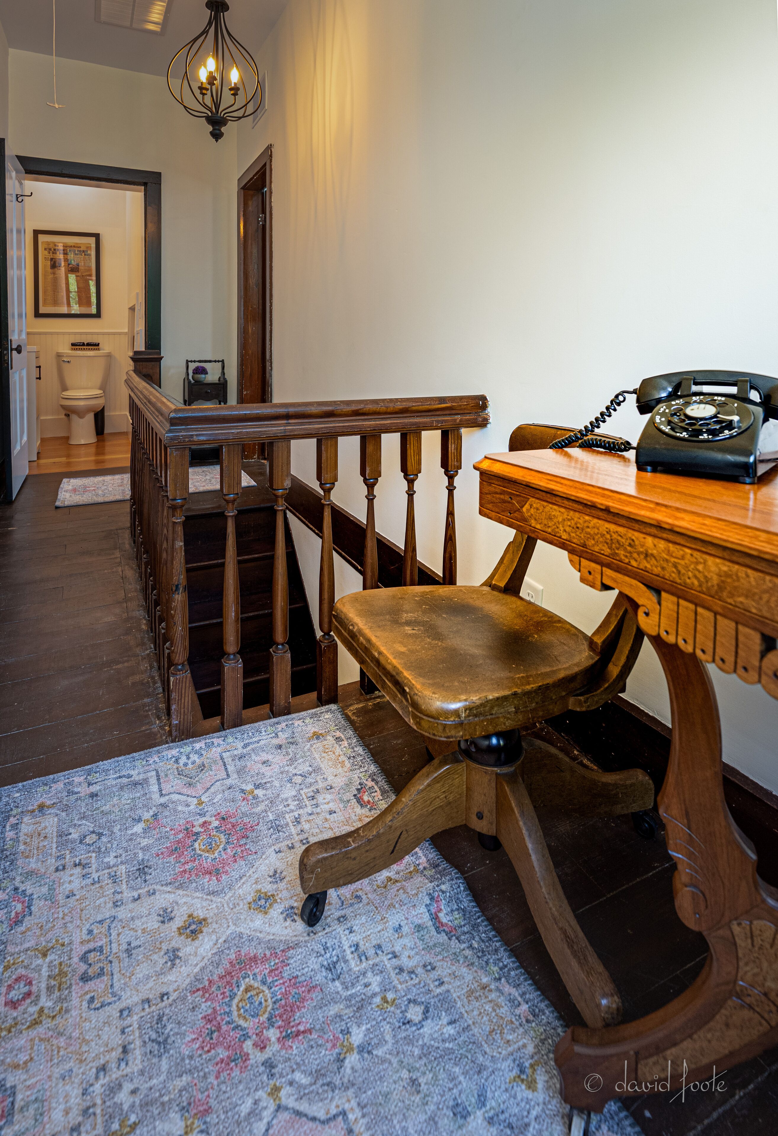 A wooden desk with a telephone, a chair, and a patterned rug in a hallway.