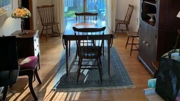 A dining area with a table and chairs, a chandelier, a cabinet, and a view through large windows.
