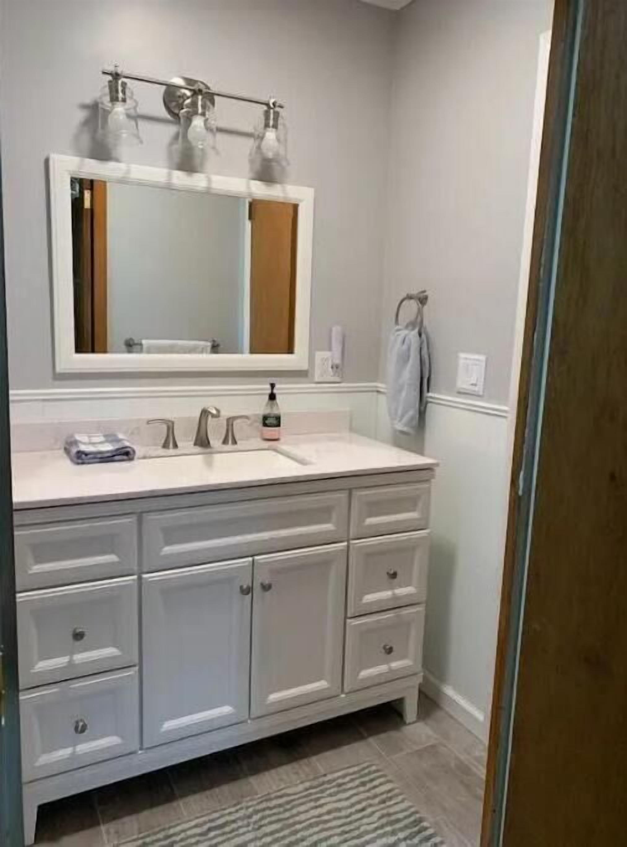 Un baño con tocador blanco, un espejo grande y un perchero para toallas.