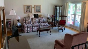 A living room with a floral sofa, a wooden coffee table, a red armchair, and a glass cabinet.