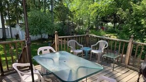 A wooden deck with a glass table and white plastic chairs.