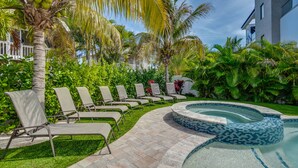 Uma área de piscina com espreguiçadeiras, hidromassagem e vegetação exuberante.