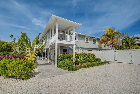A two-story house with a covered porch, a fenced yard, and tropical landscaping.