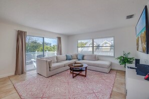 A living room with a beige sectional sofa, a patterned rug, a coffee table, and a large window with blinds.