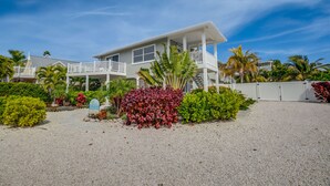 Uma casa de dois andares com uma varanda, cercada por cascalho e diversas plantas.