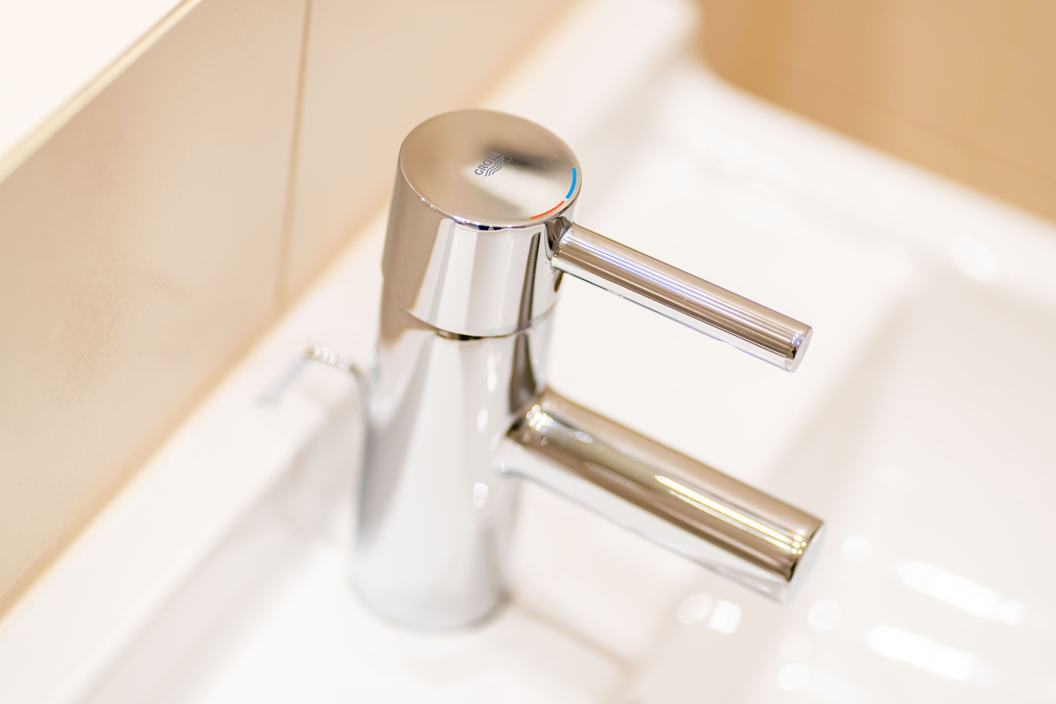Un grifo de cromo con una palanca simple y un mando lateral, instalado sobre un lavabo blanco.