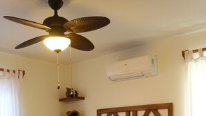 Et pænt indrettet hotelværelse med seng, loftsvifte, aircondition samt et natbord og en lampe.