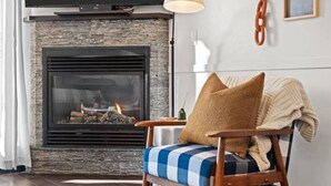 A living room with a fireplace, a television mounted above it, and a chair with a blanket.