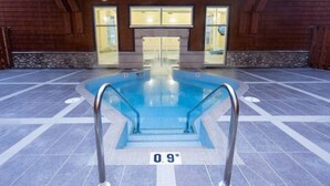 An indoor swimming pool with a 0.9m depth marker, surrounded by a tiled floor and wooden walls.