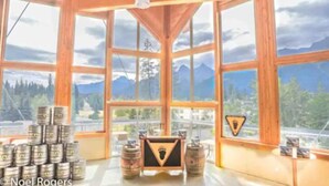 A room with large windows offering mountain views, wooden beams, and a table with barrels and a framed picture.