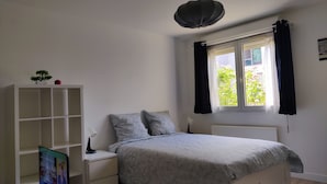 A bedroom with a bed, a nightstand, a TV, a bookshelf, and a window with curtains.
