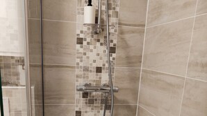 A shower with a glass door, a hand shower, and a wall-mounted soap dispenser.