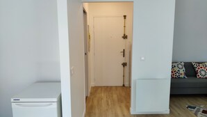 A compact living space with a kitchenette, a door leading to a bathroom, and a sofa with patterned cushions.