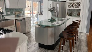 Una cucina moderna con isola centrale, sgabelli da bar, elettrodomestici in acciaio inossidabile e schienale in vetro.