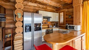 Une cuisine rustique aménagée dans une cabane en bois, avec un îlot central, des appareils en acier inoxydable et un coin repas.