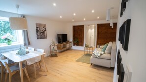 A spacious living room with a wooden floor, a white sofa, a dining table with chairs, and a television on a wooden stand. - Urlaub auf dem Bartleshof (Unterkirnach)