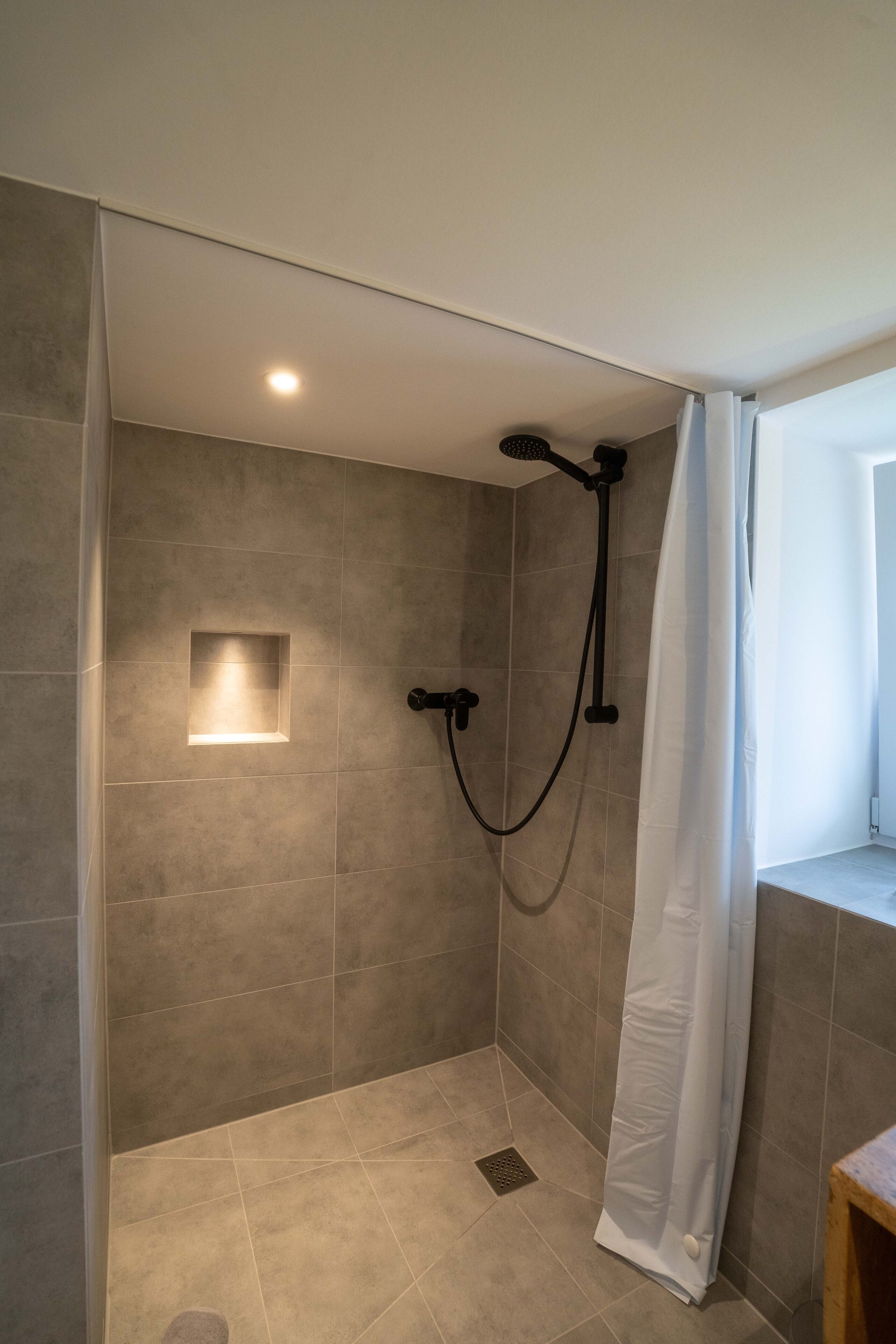 Un espace douche équipé d’un pommeau de douche à main, d’une applique murale et d’un rideau de douche blanc.