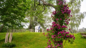A grassy area with a wooden fence, a small white building, and a tree with pink flowers. - Urlaub auf dem Bartleshof (Unterkirnach)