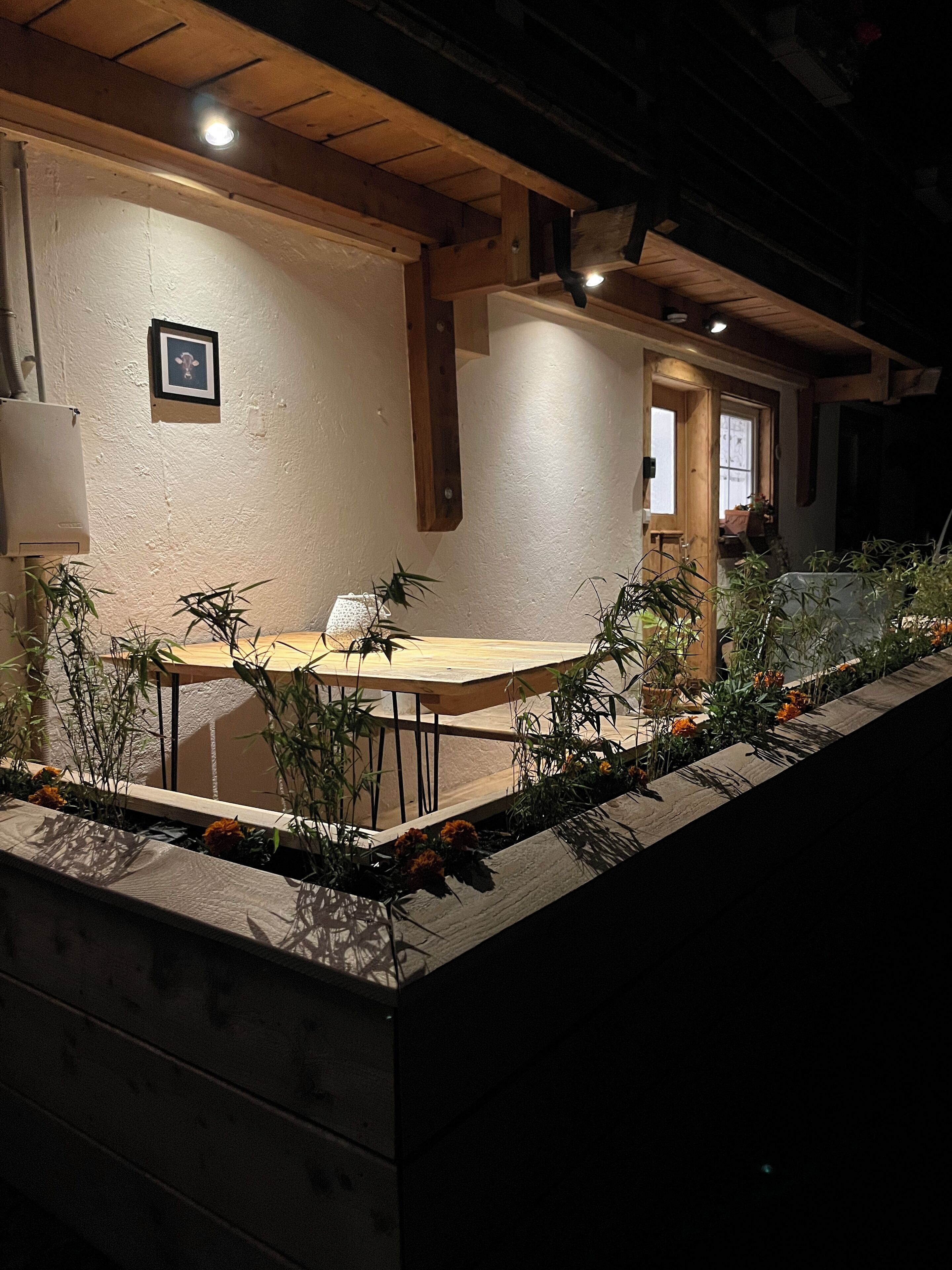 Un espace extérieur aménagé pour les repas, avec une table et des chaises en bois, entouré de plantes et de fleurs en pot.