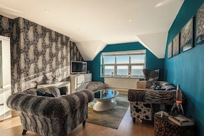 Ein modernes Wohnzimmer mit hohen Decken, einem großen Fenster mit Blick, einem Flachbildfernseher und Möbeln mit Leopardenmuster.