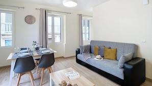 Ett modernt vardagsrum med en grå soffa, svarta stolar, ett träbord och en matplats med ett bord dukat för två personer.