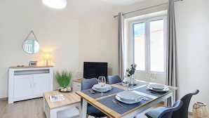 Ett modernt matområde med ett träbord dukat för två personer, en tv och ett fönster med gardiner.