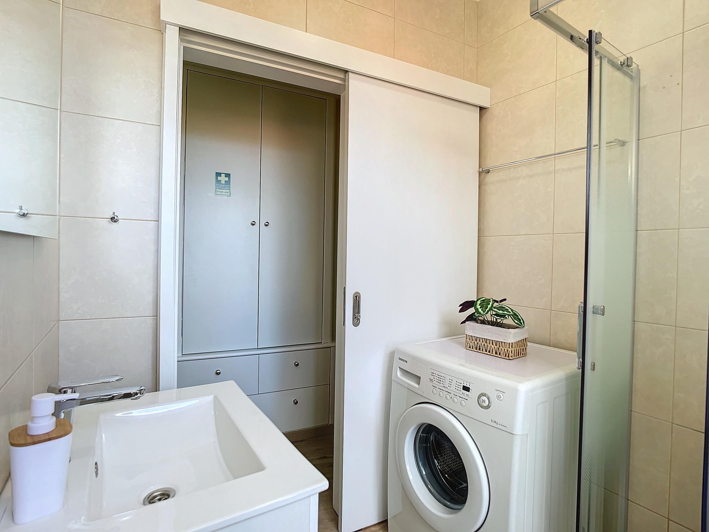 A compact bathroom with a white sink, a washing machine, and a shower enclosure.