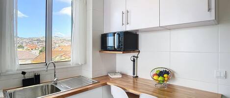 A kitchen with a window, white cabinets, a microwave, a sink, and two white chairs.