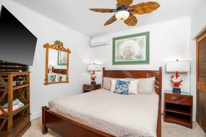 A bedroom with a wooden bed, a ceiling fan, a large mirror, a nightstand with a lamp, and a wardrobe.