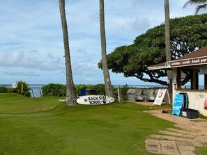 A beachside location with a surfboard sign, a beach gear rental shop, and a view of the ocean.