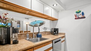 A kitchen with a granite countertop, stainless steel appliances, a wooden ceiling, and a wall-mounted decorative piece.