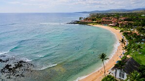 A beach resort with a curved shoreline, palm trees, and a building complex.